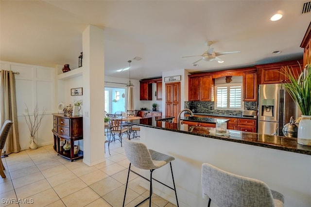 kitchen with dark stone counters, stainless steel refrigerator with ice dispenser, light tile patterned floors, pendant lighting, and decorative backsplash