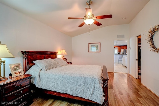 bedroom featuring light hardwood / wood-style floors, vaulted ceiling, stainless steel refrigerator with ice dispenser, connected bathroom, and ceiling fan