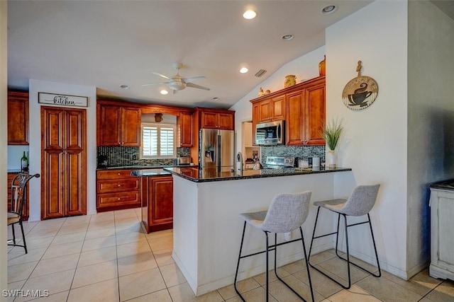 kitchen with appliances with stainless steel finishes, vaulted ceiling, dark stone countertops, and backsplash