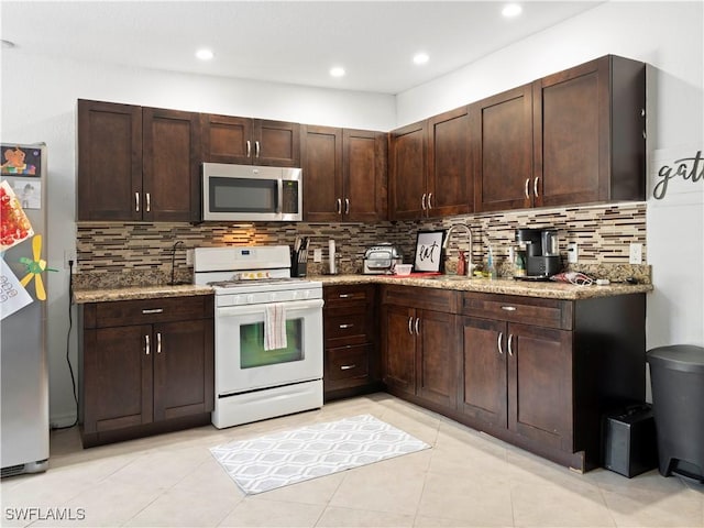 kitchen with sink, stainless steel appliances, light stone counters, decorative backsplash, and dark brown cabinets