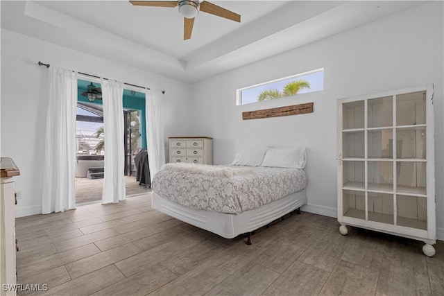 bedroom featuring ceiling fan, a raised ceiling, light hardwood / wood-style flooring, and access to outside