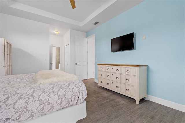 bedroom with ceiling fan, a tray ceiling, dark hardwood / wood-style flooring, and a closet