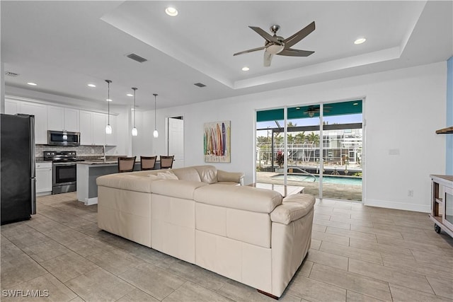 living room with ceiling fan and a tray ceiling