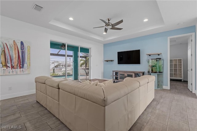 living room featuring a raised ceiling and ceiling fan