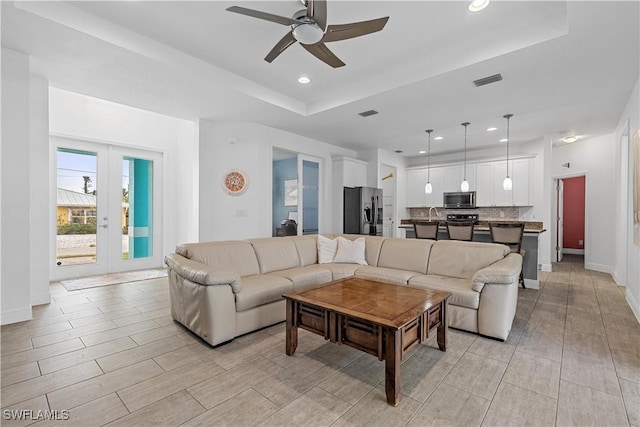 living room featuring a raised ceiling, ceiling fan, and french doors