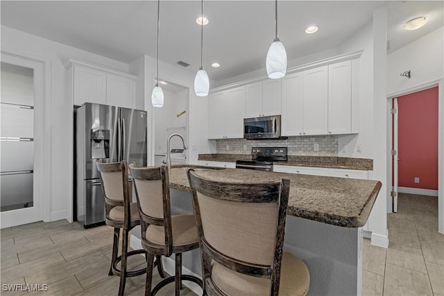 kitchen featuring stainless steel appliances, an island with sink, hanging light fixtures, and white cabinets