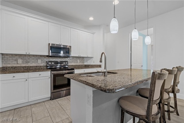 kitchen featuring pendant lighting, sink, stainless steel appliances, white cabinets, and a center island with sink