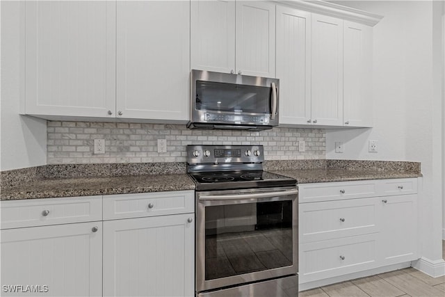 kitchen featuring stainless steel appliances, white cabinetry, decorative backsplash, and dark stone counters