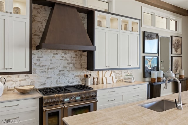 kitchen with sink, premium range hood, white cabinetry, tasteful backsplash, and range with two ovens