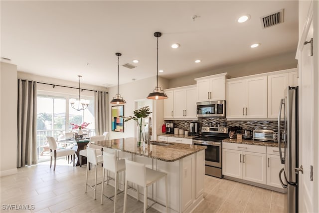 kitchen featuring white cabinets, hanging light fixtures, sink, an island with sink, and appliances with stainless steel finishes