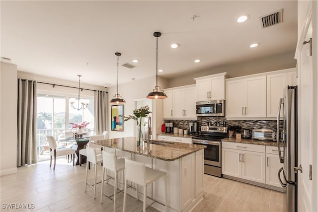 kitchen featuring sink, appliances with stainless steel finishes, white cabinetry, an island with sink, and dark stone counters