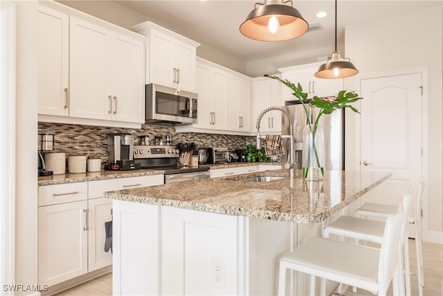 kitchen featuring white cabinets, appliances with stainless steel finishes, hanging light fixtures, and a kitchen island with sink