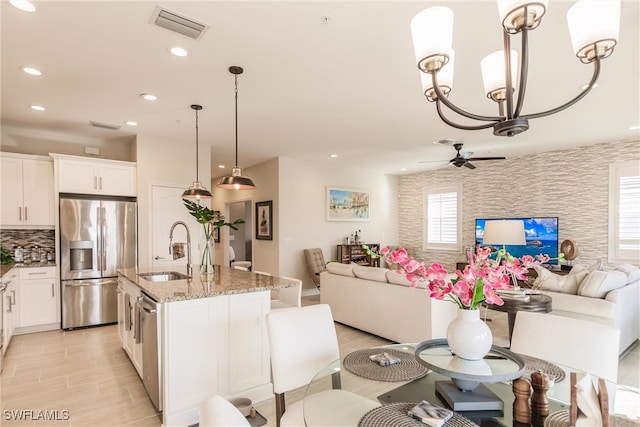 kitchen with a center island with sink, sink, stone countertops, pendant lighting, and appliances with stainless steel finishes