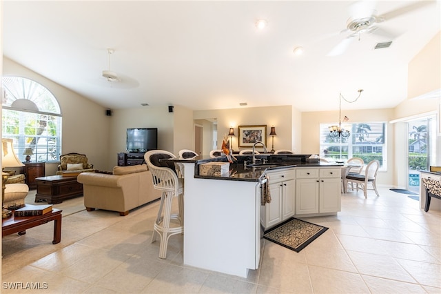 kitchen featuring ceiling fan with notable chandelier, a breakfast bar area, a kitchen island with sink, white cabinets, and pendant lighting