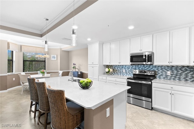 kitchen with a center island with sink, ornamental molding, white cabinetry, appliances with stainless steel finishes, and decorative light fixtures