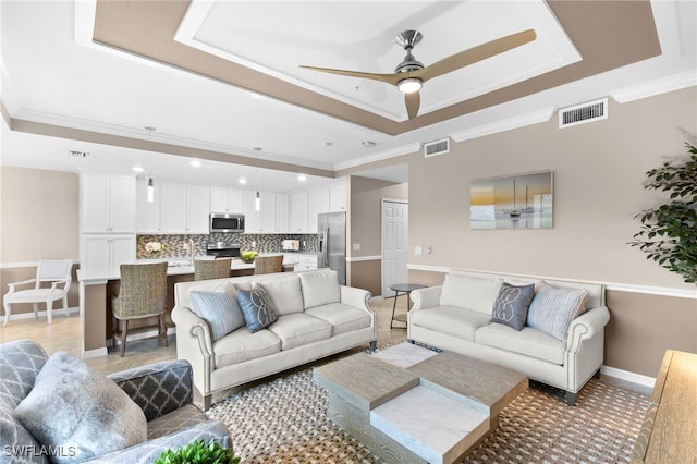 living room featuring ceiling fan, ornamental molding, and a tray ceiling