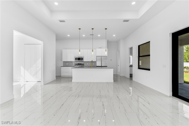 kitchen featuring stainless steel appliances, white cabinetry, tasteful backsplash, decorative light fixtures, and a kitchen island with sink