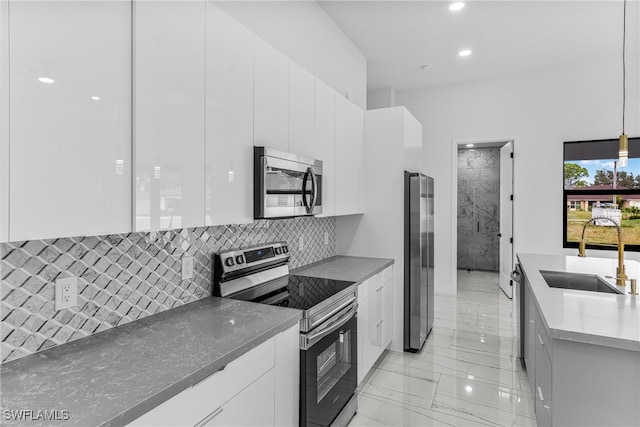 kitchen with stainless steel appliances, white cabinets, sink, backsplash, and decorative light fixtures