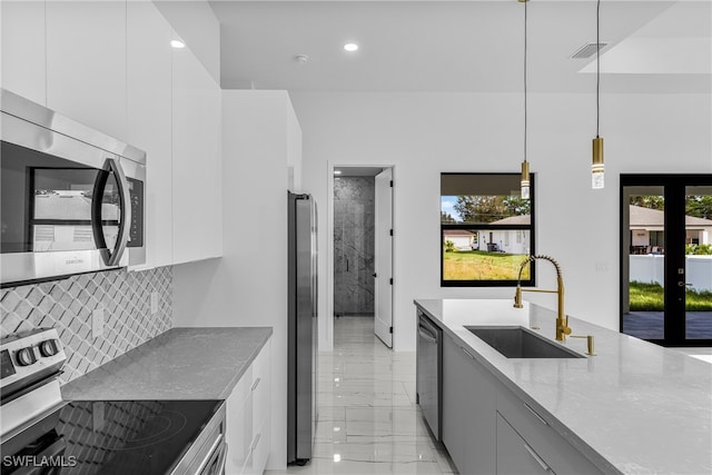 kitchen with light stone counters, stainless steel appliances, white cabinetry, decorative light fixtures, and sink