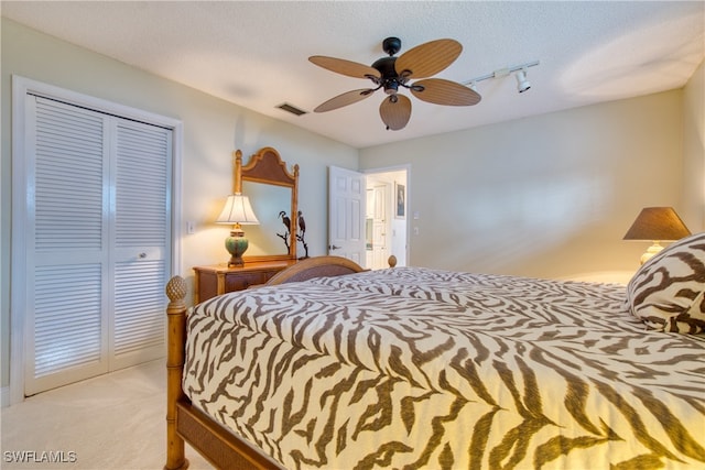 bedroom with light colored carpet, track lighting, a textured ceiling, ceiling fan, and a closet