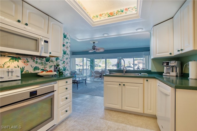 kitchen with white cabinetry, sink, ceiling fan, a tray ceiling, and white appliances