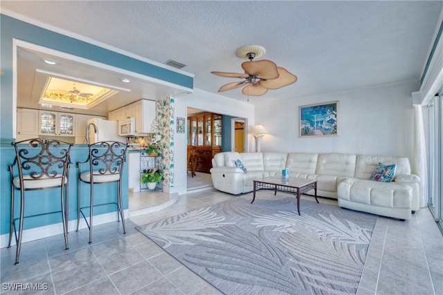 tiled living room with ceiling fan, a textured ceiling, and ornamental molding