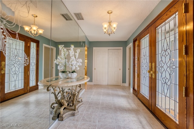 entrance foyer featuring a textured ceiling, french doors, a chandelier, and light tile patterned floors