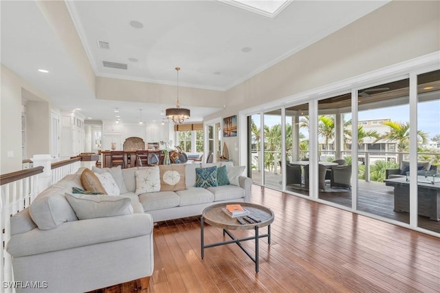 living area featuring wood-type flooring, a chandelier, visible vents, and crown molding