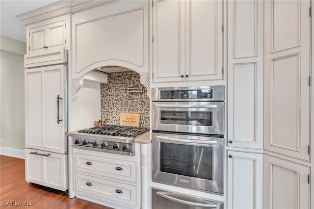 kitchen featuring light countertops, wood finished floors, a warming drawer, tasteful backsplash, and appliances with stainless steel finishes
