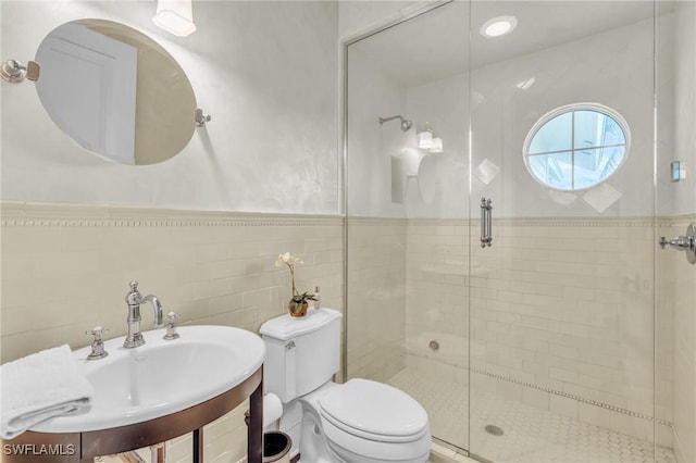 bathroom featuring toilet, a wainscoted wall, a sink, tile walls, and a stall shower