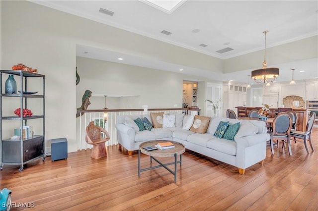 living room featuring light wood-style flooring, visible vents, and crown molding