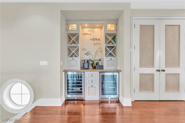 bar featuring a bar, wine cooler, baseboards, and wood finished floors