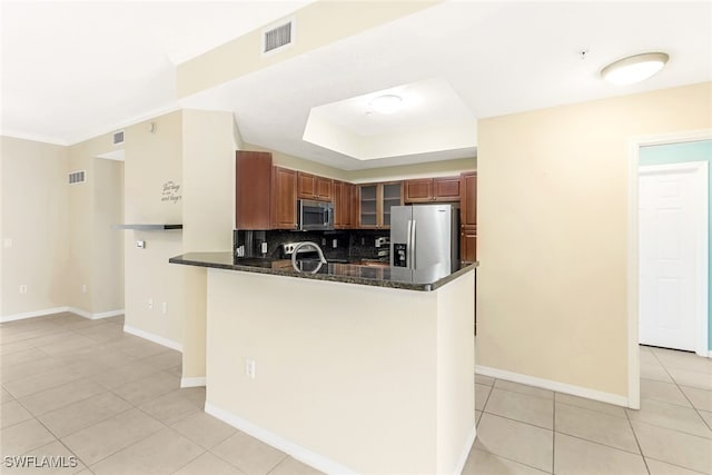 kitchen featuring dark stone counters, backsplash, appliances with stainless steel finishes, light tile patterned floors, and kitchen peninsula