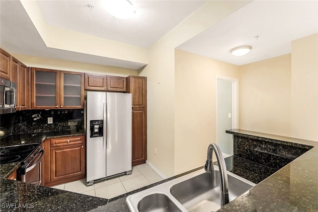 kitchen with stainless steel appliances, dark stone counters, sink, tasteful backsplash, and light tile patterned floors