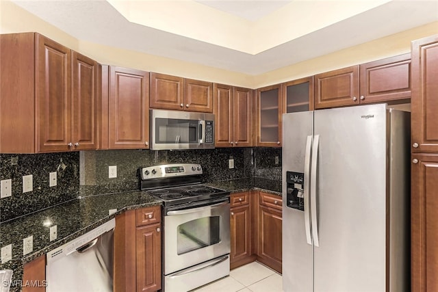 kitchen featuring dark stone countertops, backsplash, appliances with stainless steel finishes, and light tile patterned floors