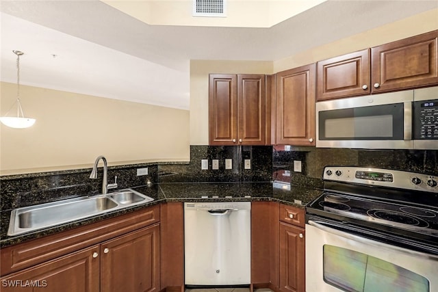 kitchen featuring sink, appliances with stainless steel finishes, dark stone counters, backsplash, and decorative light fixtures