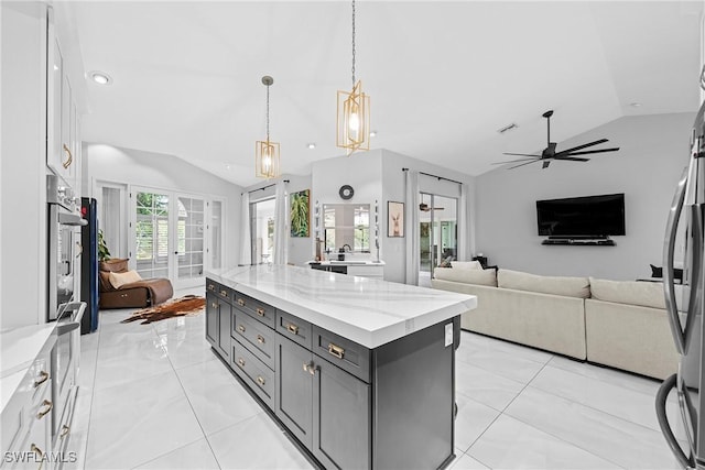 kitchen featuring french doors, lofted ceiling, a center island, decorative light fixtures, and light stone countertops