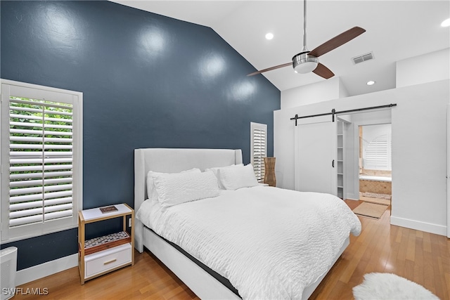 bedroom featuring ceiling fan, a barn door, light hardwood / wood-style flooring, and lofted ceiling