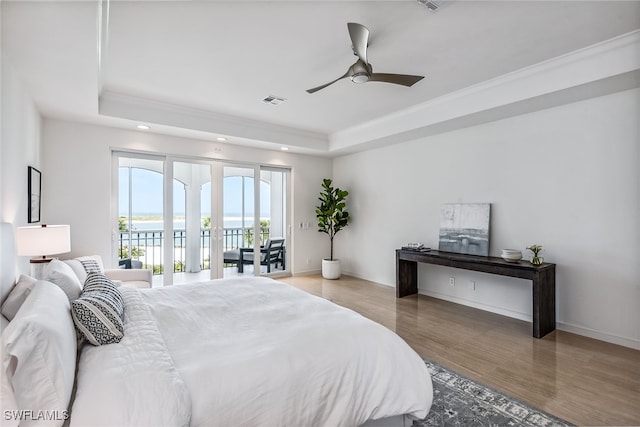 bedroom with a water view, ceiling fan, hardwood / wood-style floors, a raised ceiling, and access to outside