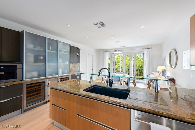 kitchen featuring stainless steel appliances, light wood-type flooring, light stone countertops, sink, and beverage cooler