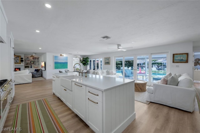 kitchen featuring sink, an island with sink, ceiling fan, white cabinetry, and light wood-type flooring