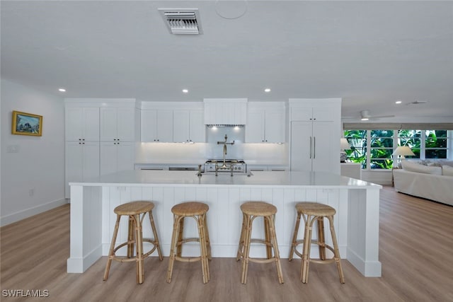 kitchen with white cabinetry, a large island with sink, light hardwood / wood-style floors, and a breakfast bar