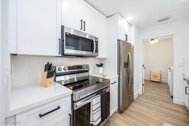 kitchen featuring washing machine and dryer, stainless steel appliances, light hardwood / wood-style flooring, tasteful backsplash, and white cabinets