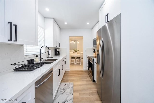 kitchen featuring appliances with stainless steel finishes, light wood-type flooring, light stone countertops, white cabinets, and sink