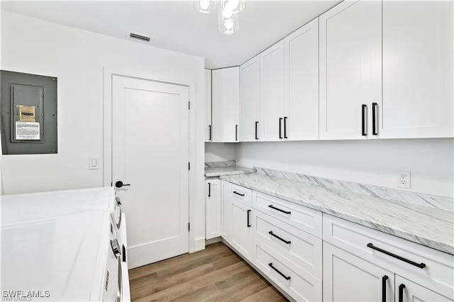 clothes washing area with electric panel, independent washer and dryer, cabinets, and light wood-type flooring