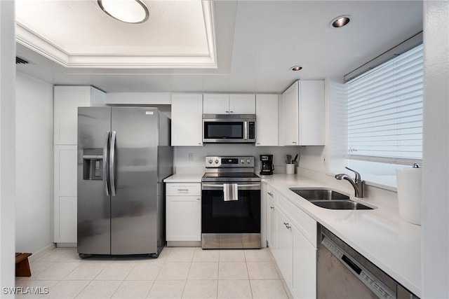 kitchen with sink, light tile patterned flooring, a tray ceiling, white cabinetry, and appliances with stainless steel finishes