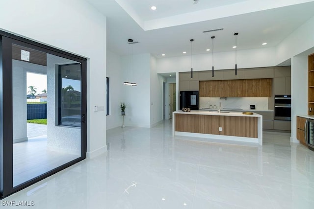 kitchen with sink, stainless steel double oven, black fridge, a large island with sink, and pendant lighting