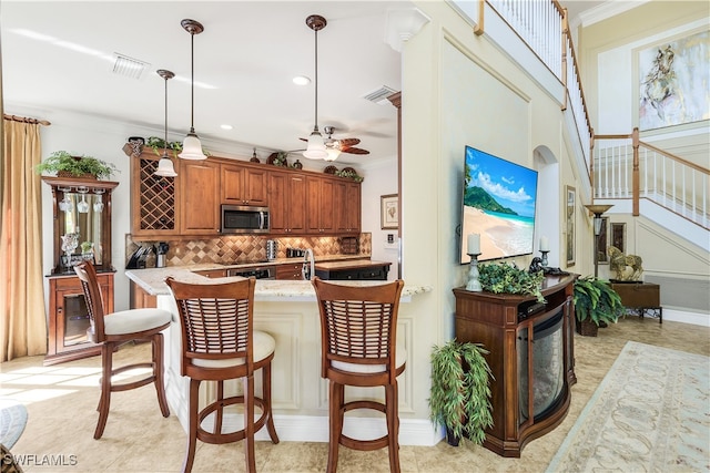 kitchen with ornamental molding, a kitchen bar, pendant lighting, kitchen peninsula, and ceiling fan