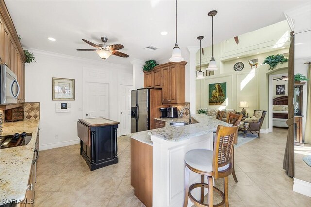 kitchen with kitchen peninsula, appliances with stainless steel finishes, light stone countertops, a kitchen island, and pendant lighting