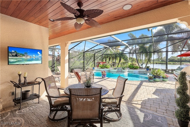 view of swimming pool with glass enclosure, a water view, a patio, and ceiling fan